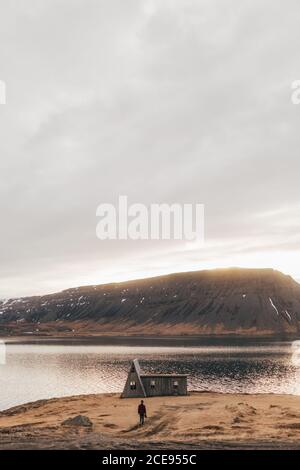 Landschaft von abgelegenen See und Haus an der Küste mit Mann zu Fuß allein in Sonnenuntergang, Island. Stockfoto