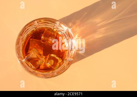 Glas kalter Whiskey auf beigem Hintergrund mit sonnigem Schatten. Stockfoto
