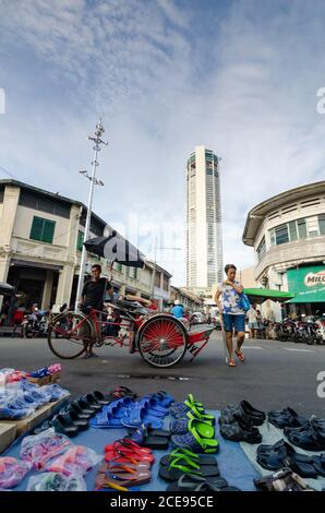 Georgetown, Penang/Malaysia - 27 2016. August: Ein Trishaw-Fahrer rast vor dem Showstand. Hintergrund ist das KOMTAR-Gebäude. Stockfoto