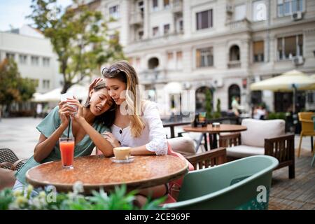 Depressive junge Frau hält Handy, während sie getröstet wird Ihr Freund Stockfoto