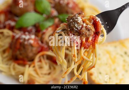 Spaghetti und Fleischbällchen auf einer Gabel mit Spaghetti auf einem Platte im Hintergrund Stockfoto