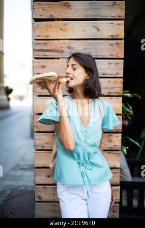 Schöne junge Frau, die draußen ein Stück Pizza isst Stockfoto