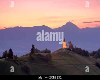 Sonnenaufgang über einer Kirche in Jamnik in den Julischen Alpen. Stockfoto