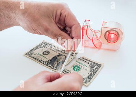 Nahaufnahme der Hände eines Mannes, der alte, zerrissene Dollarbriefe repariert Mit Klebeband auf weißem Schreibtisch Stockfoto