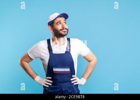 Nachdenklicher Handwerker in Overalls, der aufschaut, mit glücklich inspiriertem Ausdruck träumt, Wunsch machend. Beruf der Dienstleistungsbranche, Kurierdienst, ho Stockfoto