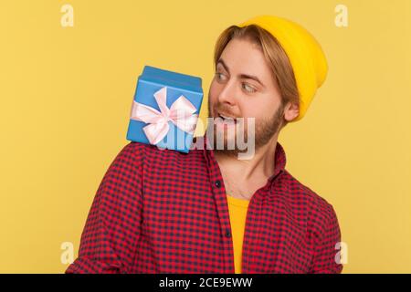 Lustige optimistische Hipster Kerl in Beanie Hut und karierte Shirt Blick schockiert auf Geschenkbox auf seiner Schulter, überrascht von plötzlich gefunden Geburtstag prese Stockfoto