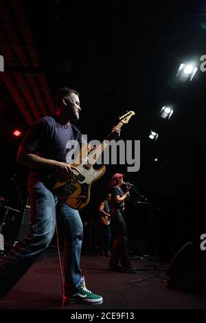 Caucasian man ist auf der Bühne mit Band. Handsome Male Person spielt auf Bass Gitarre bei Concert. Stockfoto