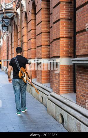 Man ist zu Fuß entfernt mit Bass Guitar auf Fußgängerstraße Gehweg. Stockfoto