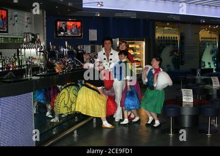 Glasgow Prestwick Airport Ayrshire im Vereinigten Königreich ist der einzige Ort, der von 'The King of Rock & Roll' l Elvis Preseley geführt wird. Im Geburtsdienst wurde Sergent Presley am 3. März 1960 von kreischenden Fans begrüßt, nachdem sein Flugzeug zum Tanken angehalten hatte : Foto zeigt Elvis Presley ( aka Gordon Hendricks Gewinner der ITV Stars in Their Eyes 2005 ) in der Elvis Bar Glasgow Prestwick Airport mit Fans Stockfoto