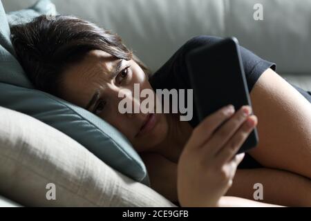 Traurige Frau, die im Dunkeln telefoniert und auf einem liegt Sofa im Wohnzimmer zu Hause Stockfoto