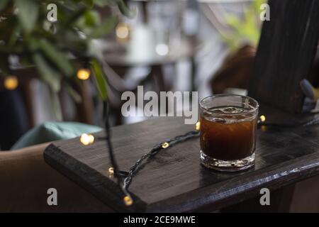 Selektive Fokusaufnahme eines Glases schwarzen Eiskaffees Auf einem Kaffeetisch mit Lichtern Stockfoto