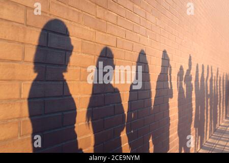 Eine Linie der Schatten von Menschen säumten gegen ein Red brick wall. In einer Warteschlange, um die Änderungen zu stehen Stockfoto