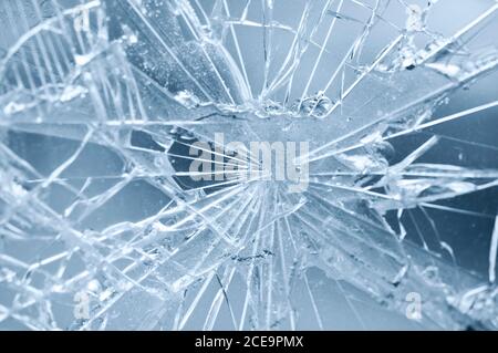 Unfall - Nahaufnahme eines kaputten Fensters. Detail der Risse von rissenen Glas. Blauer Hintergrund. Stockfoto