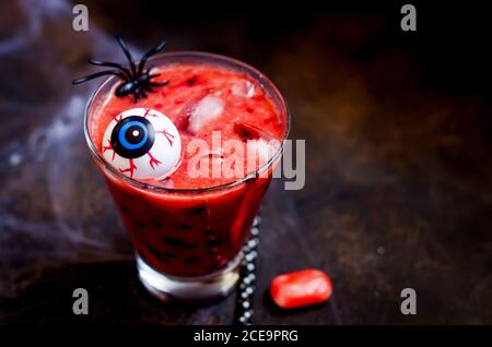 Roter Beerencocktail mit Eis, Augen und Spinnen für halloween Party auf dunklem alten Holztisch mit Netz. Herbst Halloween Feiertagskonzept, Vorlage guardia Stockfoto