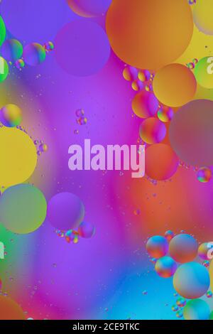 Makrofoto des Mischens von Öl und Wasser. Öltröpfchen über einem schönen farbigen abstrakten Hintergrund schaffen Kreise und Ovale. Stockfoto