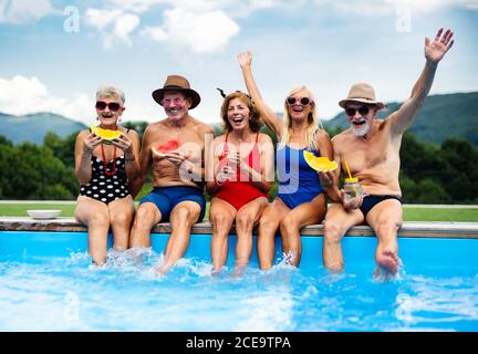 Gruppe von fröhlichen Senioren sitzen am Pool im Freien im Hinterhof. Stockfoto
