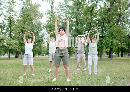 Eine Gruppe älterer Menschen und ihr Coach heben die Arme hoch Während der Dehnung Körper im Outdoor-Fitness-Klasse Stockfoto