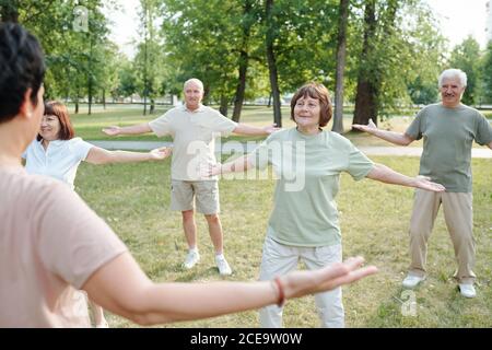 Rückansicht des Qigong-Lehrers, der die Arme während des Unterrichts ausgestreckt hält Ältere Menschen tief atmen Stockfoto