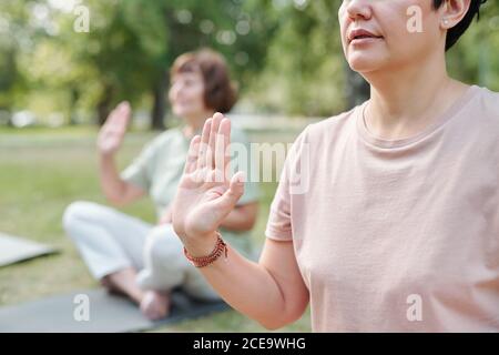 Nahaufnahme von Frauen, die im Freien in Asana sitzen und Yoga-Übungen durchführen, halten sie die Hände und sagen Gelübde Stockfoto