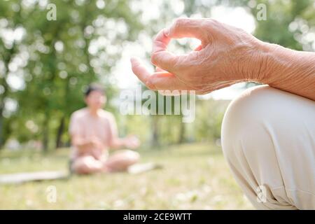 Nahaufnahme eines nicht erkennbaren älteren Mannes, der während der Mudra die Hand hält Meditation in der Gruppe Yoga-Kurs im Freien Stockfoto