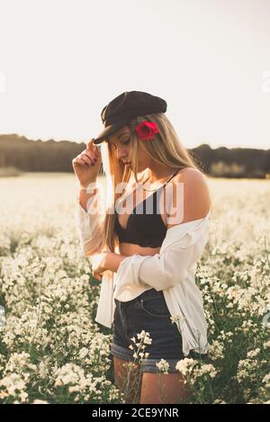 Junge Dame mit schwarzer Mütze und Mohn in Haaren posiert In dunklen BH in Blanche Blumen Stockfoto