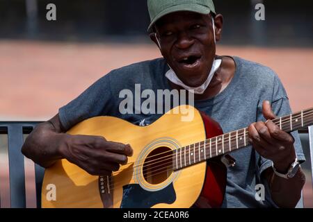Annapolis, MD 08/21/2020: Ein älterer afroamerikanischer Mann, der Baseballhut und eine Gesichtsmaske trägt, spielt klassische Gitarre und singt, während er o sitzt Stockfoto