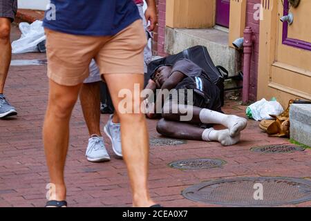 Annapolis, MD 08/21/2020: Ein obdachloser afroamerikanischer Mann schläft auf dem gepflasterten Bürgersteig auf seinem Gepäck. Seine Kleider sind Dorn aus und schmutzig. Stockfoto