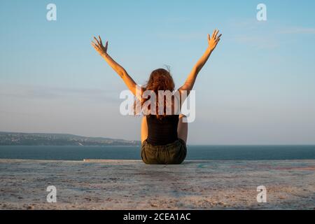 Rückansicht einer jungen Dame, die an einem Betonufer sitzt und die wunderschöne Aussicht auf das ruhige Meer an einem windigen Tag in Bulgarien, Balkan, bewundert Stockfoto