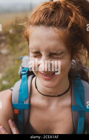 Hübsche junge Frau mit Rucksack lächelnd und schielend, während sie auf unscharfem Hintergrund der Natur in Bulgarien, Balkan, steht Stockfoto