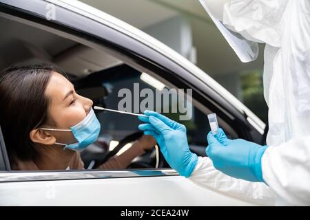 Portrait der asiatischen Frau Drive thru Coronavirus covid-19 Test durch medizinisches Personal mit PSA Anzug von Nase Tupfer. Neue normale Gesundheitsversorgung Drive-Thru-Service und Stockfoto