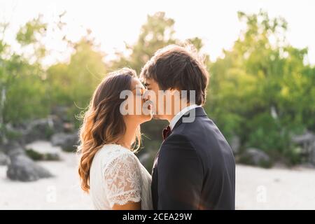 Ein Paar in Hochzeitskleider, die auf Felsen stehen und sich glücklich umarmen Gegen grüne Bäume und blauen Himmel Stockfoto