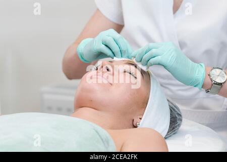 Die junge Kundin des Kosmetiksalons mit einem Gesichtsreinigungsverfahren. Der Arzt Kosmetologe Reinigung der Haut mit Schwamm. Konzepte der Hautpflege Stockfoto