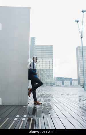 Afroamerikanischer Geschäftsmann, der sich im Freien an einer Wand lehnt Stockfoto