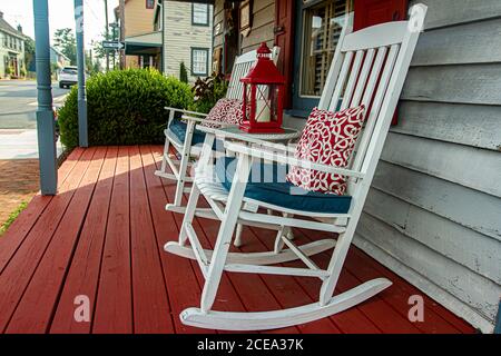 Chesapeake City, MD, USA 08/25/2020: Nahaufnahme von zwei traditionellen weißen Holzschaukelstühlen auf einer rot bemalten Veranda eines amerikanischen H aus dem 19. Jahrhundert Stockfoto