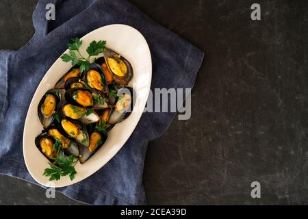 Keramikplatte mit leckeren gekochten Muscheln stehen auf Stück Tuch auf grauem Hintergrund Stockfoto