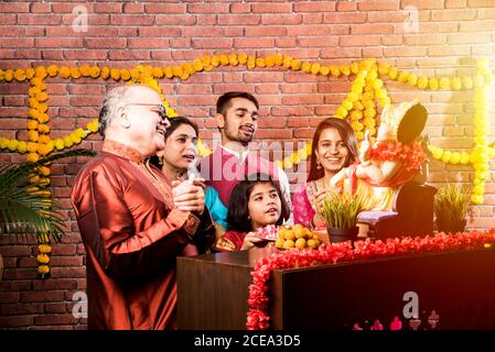 Happy Indian Family feiert Ganesh Festival oder Chaturthi - einladend Oder Pooja und Süßigkeiten in traditioneller Kleidung zu essen Haus eingerichtet w Stockfoto