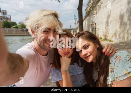 Schöne junge Frauen in legerer Kleidung und trendigen Mann fotografieren Von sich selbst im Freien Stockfoto