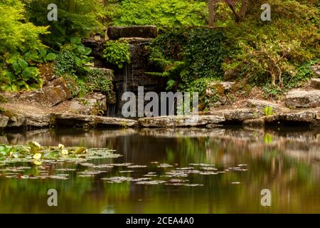 Eine lange Belichtung Bild von einem dekorierten Garten Teich mit Seerosen und einem kleinen Wasserfall, wo Wasser fließt über glatte Felsen in den Pool. Das ar Stockfoto