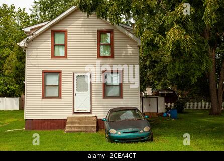 Chesapeake City, MD, USA 08/25/2020: Ein altes kaputtes rostiges Auto mit nebligen Scheinwerfern wird vor einem Einfamilienhaus mit großem Hof zurückgelassen. Das ist es Stockfoto