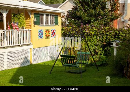 Chesapeake City, MD, USA 08/25/2020: Eine grüne, alte Metallgartenschaukel auf dem Vorgarten eines traditionellen amerikanischen Hauses im alten Stil mit Holzshutte Stockfoto