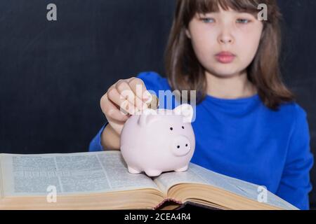 Teen legt Münzen in das Sparschwein. Das Konzept der bezahlten Bildung Stockfoto