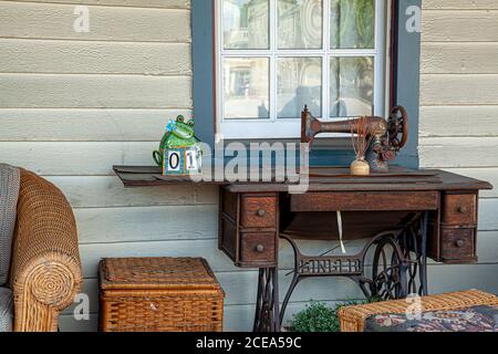 Chesapeake City, MD 08/25/2020: Nahaufnahme einer rostigen antiken Handkurbel Singer Nähmaschine vor dem Fenster auf der Veranda eines ol platziert Stockfoto