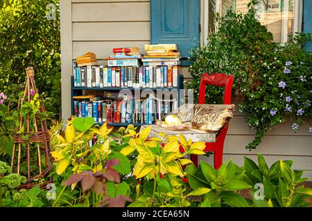 Chesapeake City, MD, USA 08/25/2020: Ein Bücherregal voller Bücher verschiedener Genres befindet sich auf der Veranda eines alten Hauses. Ein Schild mit der Aufschrift „Hilf dir Stockfoto