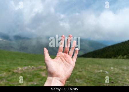 Crop Hand mit winzigen Marienkäfer auf Finger auf dem Hintergrund Grüne Sommerlandschaft mit Bergen in Wolken Stockfoto