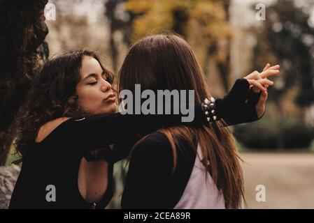 Langhaariger Mann umarmt und küsst Frau in der Nähe von Baum Stockfoto
