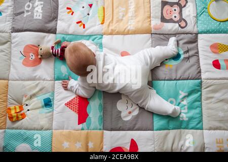 5 Monate altes Baby, das auf einer Spielmatte liegt und nach einem Spielzeug greift Stockfoto
