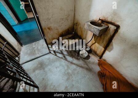 Kleines grungiges Waschbecken, das an einer Betonwand in der Nähe einer offenen Tür von Dirty im Gefängnis in Oviedo, Spanien, befestigt ist Stockfoto