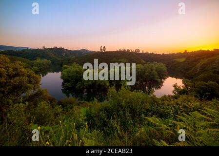 Panoramablick auf den ruhigen Nora Fluss, der langsam zwischen grünen Bäumen im Hochland in der Sonnenuntergangszeit fließt, Spanien Stockfoto