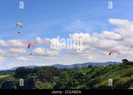 Herrliche Drohnenansicht von hellen Gleitschirmen, die gegen den bewölkten Himmel fliegen Über schöne grüne Natur an sonnigen Tagen Stockfoto