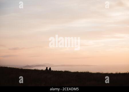 Rückansicht von Jungs sitzen auf Gras und Blick malerischen Sonnenuntergang am Himmel Hintergrund in Kantabrien, Spanien Stockfoto